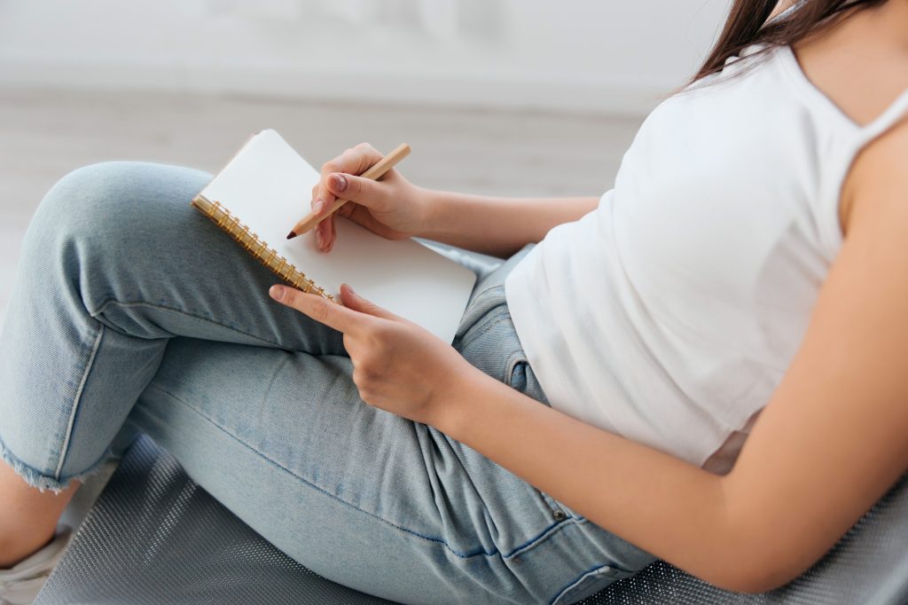 Side view of hand young brunette holds pen and notebook in home interior. Writer concept. Copy space